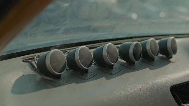 A smooth cinematic pan across a row of dusty, weathered aftermarket gauges mounted on the dashboard of an abandoned vintage car in bright daylight.