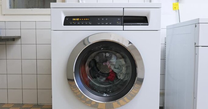 Static video of a white front-loading washing machine with colorful clothes spinning in the drum. Close up shot, real time video, no people