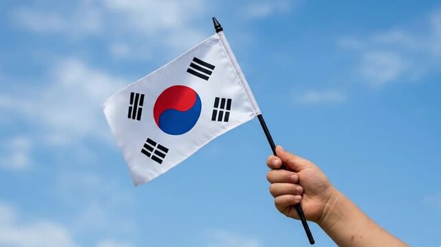 Child hand holding the South Korean national flag against a bright blue sky for Independence Day celebration