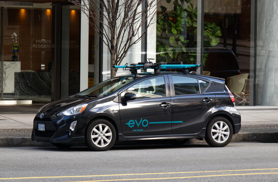 An Evo Car Share branded Toyota Prius with roof rack parked on a downtown Vancouver street near a residential lobby