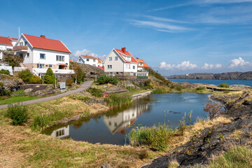 Fototapeta premium White wooden houses with red roofs beside small pond on Övre Åledammsvägen in Åstol, Bohuslän, west coast Sweden