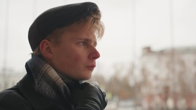 White man creator in urban portrait, closeup of pensive young artist wearing wool cap and scarf, winter coat, overcast light, contemplative gaze toward city, cinematic moody atmosphere