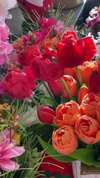 Vertical vibrant bouquet mixed flowers in shop, close detail showing pink hydrangea, red carnation and orange tulip clusters among green foliage. Plastic decorative flowers arranged indoors.