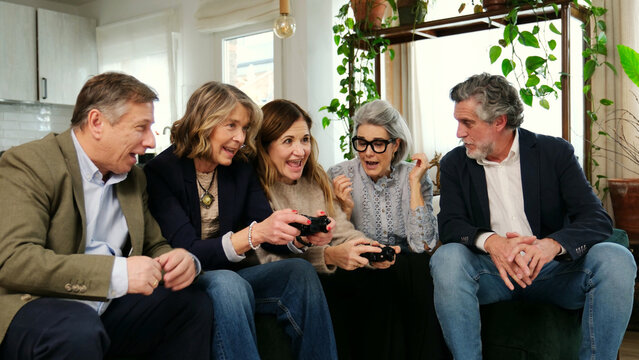 Happy mature friends having fun playing video games in a living room