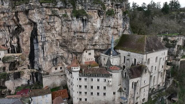 Aerial view of Rocamadour dramatic stone buildings and church perched directly on vertical cliff face with valley below