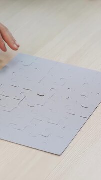 A man is assembling a puzzle on a smooth table. His hands are placing a puzzle piece into the incomplete puzzle, focused on the puzzle's arrangement.