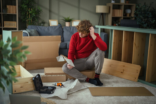 Young man assembling flat-pack furniture at home following instructions