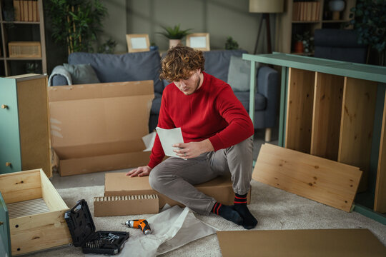 Young man assembling flat-pack furniture at home following instructions