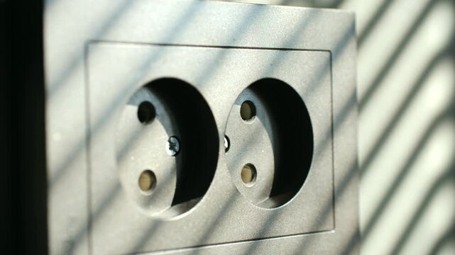 Person unplugging a white charger from a gray wall outlet to disconnect a device and save electricity, illustrating energy conservation and reducing household power consumption costs