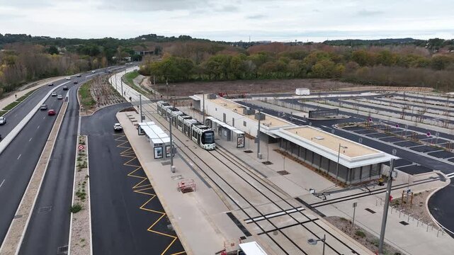 Aerial view of Montpellier tramway modern tram with green pattern stopped at platform near road and parking area with trees