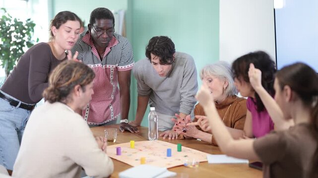 Engaged men and women of different ages playing tabletop game during interactive workshop indoors