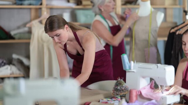 Team of female dressmakers with a fashion designer work in the sewing industry. Mature seamstress sews clothes against the background of young assistants. Master class in the atelier