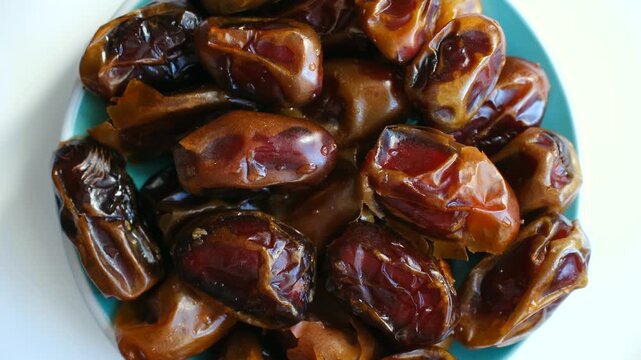 Shiny, ripe, and sweet date fruits rotating on a turquoise plate isolated on a white background. This healthy, vegan, and raw food is a perfect natural dessert and a great source of energy
