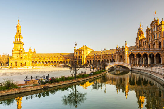 Travel, tourism: Plaza de Espa&ntilde;a architecture reflects in the water, people walk around the landmark in Seville, Spain. Plaza de Espa&ntilde;a, Seville, Spain.