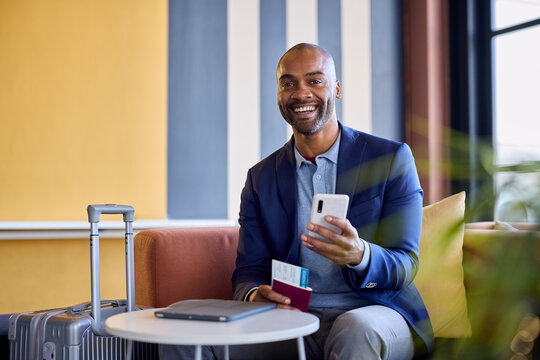 Happy mid adult black business man at airport using smartphone