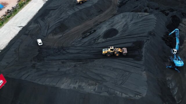 Aerial view of a massive excavator loading coal into a pile in an open pit. Heavy machinery operating in a precise rhythm, industrial coal mining on a large scale in bright daylight. 4k footage