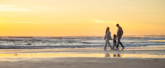 Family walking along beach at golden hour sunset