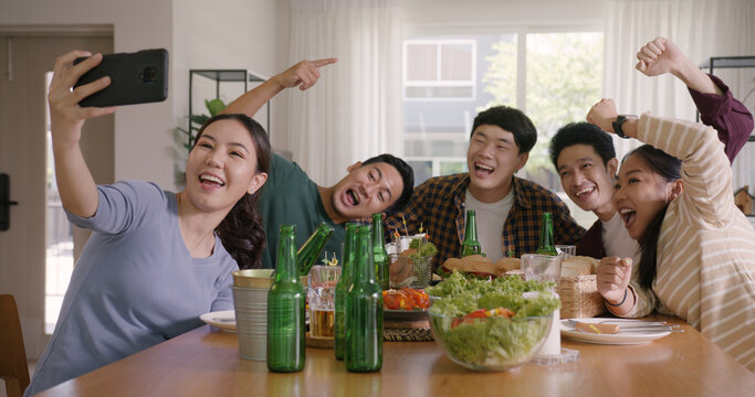Happy hour diner at home relax smile look at camera shooting video photo on mobile app. Group of asia people young adult friend man and woman sit at dining table joy fun talk or eat food drink beer.
