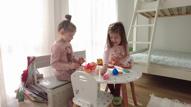 Cute little girls playing with plastic toy kitchen indoors at home.