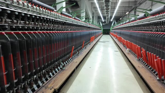 Industrial textile spinning machine with colorful yarn spools inside a factory, automated thread production line. Manufacturing equipment from a traditional wool or cotton mill.
