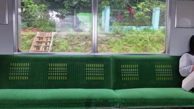 Train interior with patterned green seats and window view of passing trees and greenery