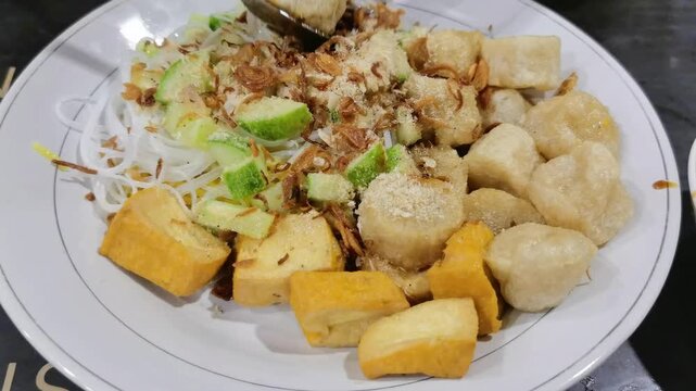 Indonesian pempek empek empek dish with noodles tofu crackers cucumber and savory sauce close up