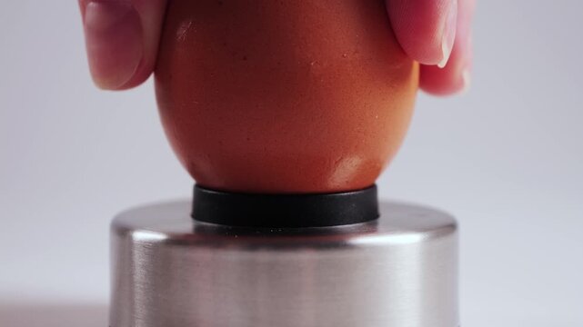 A hand holds a chicken egg and carefully pierces the shell using an Egg piercer, egg pricker. The small hole helps prevent cracking during boiling and makes peeling easier after cooking. High quality