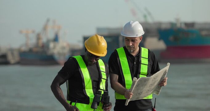 Engineer and technician review port operations and coastal logistics beside the waterfront in daylight, supporting maritime planning, cargo monitoring, and harbor infrastructure assessment.
