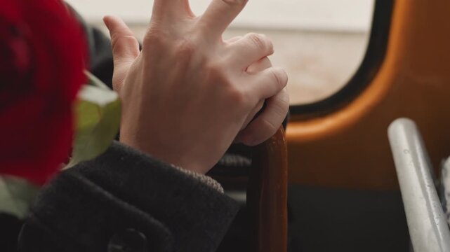 Detailed descriptive scene. Person gripping wooden handle with rings. Nervous individual holding cane near blooming rose with rings. Closeup of person fidgeting with vintage accessory by window