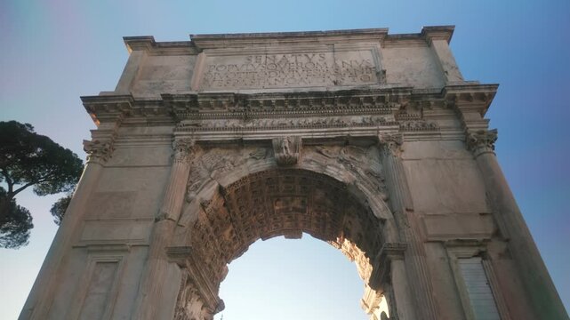 A smooth cinematic push-in shot of the historic Arch of Titus in the Roman Forum, Rome. Features detailed Roman relief carvings, ancient Latin inscriptions (SPQR), and warm golden hour light.