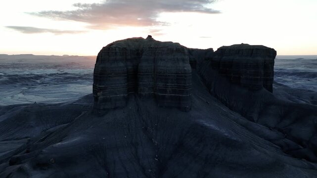 Aerial view of stark, layered cliffs etched by time stand in silhouette against a pastel dawn sky, Utah, United States.
