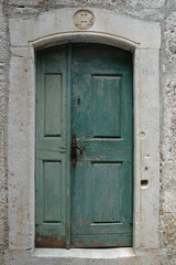 Fototapeta premium A weathered green wooden door is framed by a limestone portal featuring a carved IHS (Iesus Hominum Salvator) religious monogram in the old town of Korcula