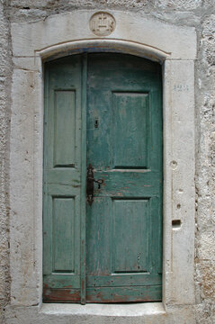 A weathered green wooden door is framed by a limestone portal featuring a carved IHS (Iesus Hominum Salvator) religious monogram in the old town of Korcula