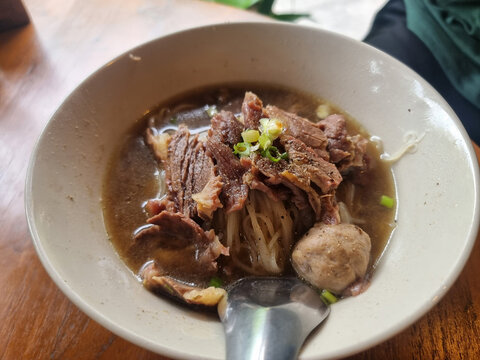 Authentic Thai beef noodle soup (Kuay Teow Neua) served in a bowl on a wooden table at a local restaurant.