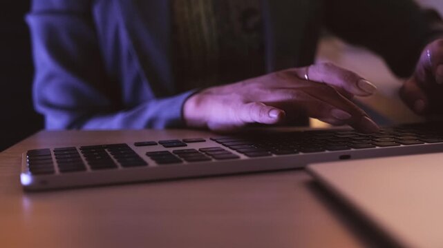 Close-up of a hand typing on a keyboard at a desk in low light, suggesting late-night office work or coding