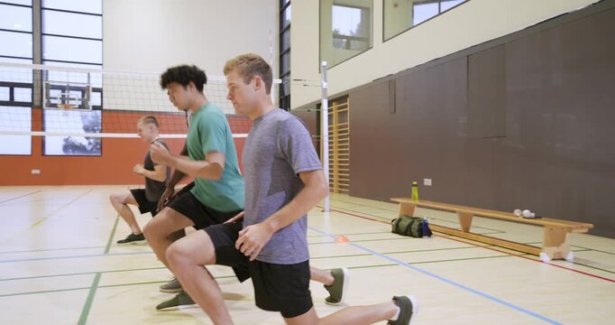 Drill start Diverse men in shorts warming lunges shuffles sprints in school gym by volleyball net