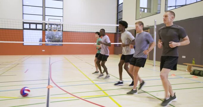 Diverse male teammates reacting to cue, starting footwork drill for warm-up on gym court with cones