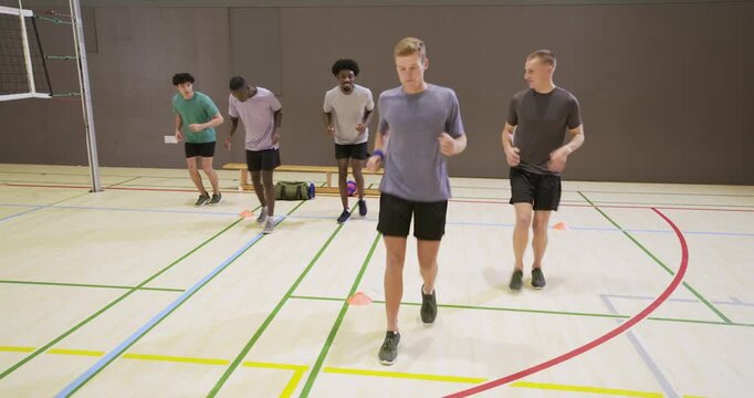 Diverse male teammates on cue performing footwork drill in gym over court lines near cones