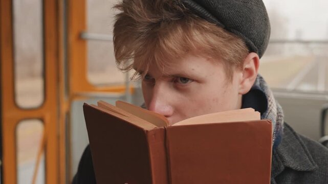 Young white actor creator rehearsing lines tram, closeup with hardcover book as script, intense gaze, furrowed brow, performance practice, vintage carriage backdrop, focused creative energy