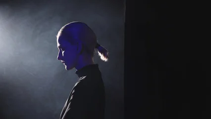 A young blonde woman with a short ponytail steps into a powerful side light. High-contrast video with her thoughtful profile illuminated, symbolizing the decision to stop being silent and embrace publ © Ulia Koltyrina