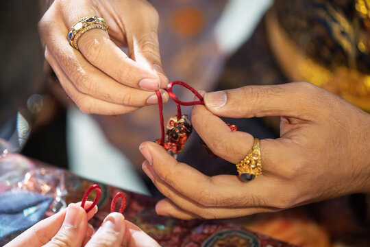 Person wearing gold ring holds red string and Thai keychain