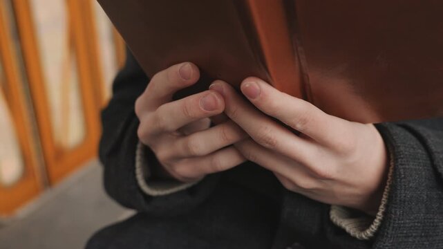 White creator closeup hands examining binding, leather cover and visible stitches, gentle thumb motion flipping pages, tactile paper texture and grain, artisan study vibe on vintage tram, focus