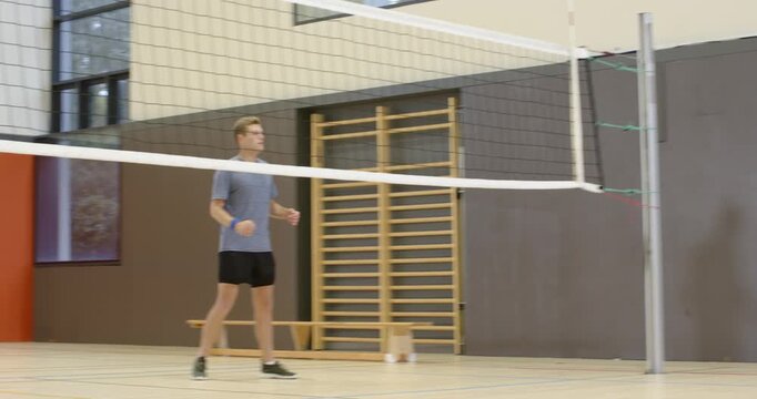 Diverse male team lunging, blocking at net in school gym after opponent serve, shaking hands