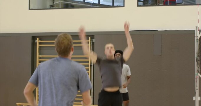 Diverse male team moving to incoming volleyball, blue pushing up, blocker leaping, playing