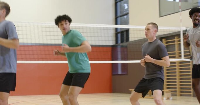 Diverse adult male players starting warmup drill, jogging and doing footwork along volleyball net