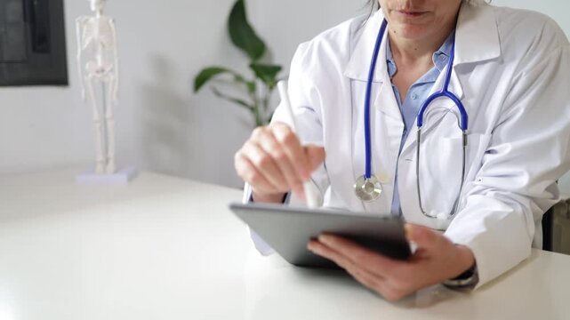 Female doctor using a digital tablet with a stylus in a modern hospital office, focused on managing patient records and integrating electronic health record technology