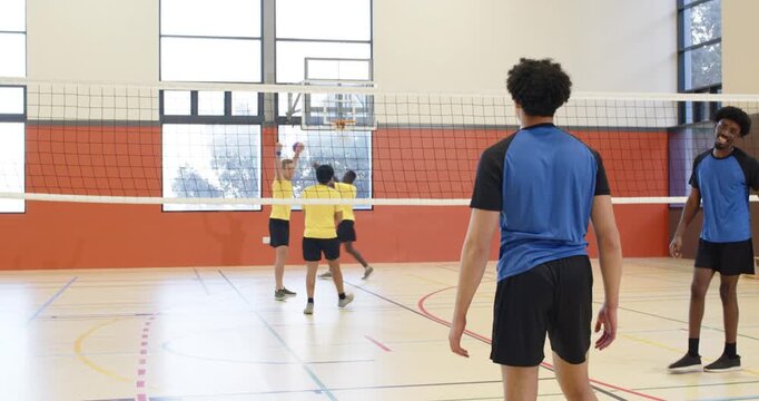 African American man in blue tee receiving yellow serve jumping spiking scoring in gym, copy space