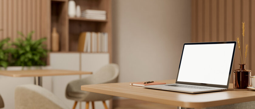 White screen laptop and books aside flower vase on wooden table with chair in a living room or cafe.