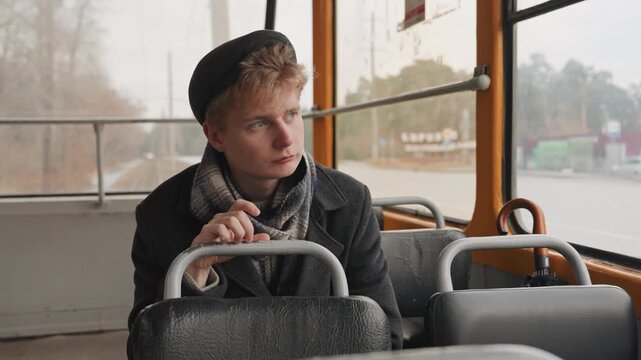White creator on tram gazing forward and holding seat, frontal frame shows attentive expression and quiet planning young white artist and storyteller studies passing city, fingers on handle, subtle