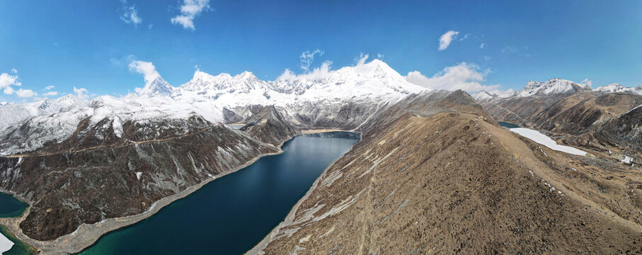 Epic wide panorama of snow covered Kula Kangri mountains and alpine lake Tibet China